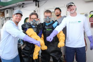 The RECOVER team suits up in safety gear to protect them while transferring oil-exposed mahi-mahi from the recovery tanks into the Gulf of Mexico. Here, Principal Investigator Dr. Martin Grosell (middle) and Ph.D. student and cruise lead scientist Lela Schlenker (left of Martin), are ready to enter the recovery tank and navigate the tagged mahi into a vinyl sling. Then, Dr. John Stieglitz (far left), Ron Hoenig (far right), and Ph.D. student CJ McGuigan (grey shirt) will release the mahi-mahi from the stern of the Walton Smith into the Gulf of Mexico. Photo credit: RECOVER consortium.