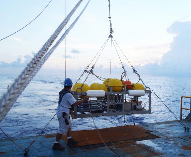 OLYMPUS DIGITAL CAMERA The injection sled is equipped and ready for deployment from the RV Brooks McCall. The white bumpers provide buoyancy for recovery. The grey horizontal tubes, next to engineer Brian Guest, sample salinity to calibrate the CTD behind them. The tracer reservoirs (center) have batteries that run the injectors. The yellow “hard hats” encase hollow glass spheres, making the sled neutrally buoyant as it streams behind a cable when towed at 1 knot. (Photo credit: Laura Spencer)