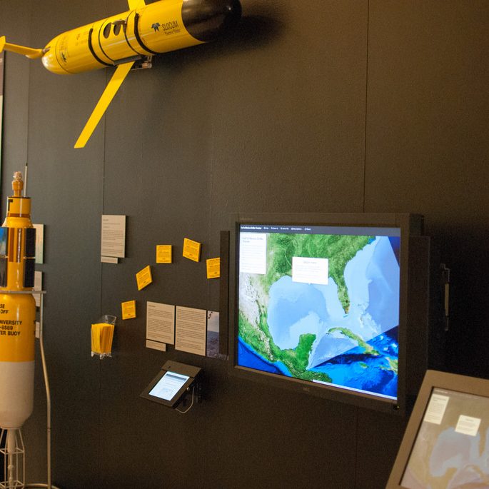 GISR_BushLibraryExhibit_GliderCardsDisplay Some of GISR-related research on display at the Bush Library: standing is 1/4 scale replica of an automated monitoring buoy; mounted on the wall is a full-sized ocean glider, GISR Driftcards and bookmarks with an interactive map of the Gulf of Mexico to view their dispersion; and an interactive “Make Your Own Oil Spill” visualization. (Photo courtesy of Bush Library)