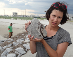 Helen White on a Gulf coast beach holding a jetty rock with oil residue on it. (Image: Mike McNulty, Woods Hole Oceanographic Institution)