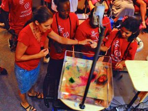 Professor Josefina Olascoaga assists camp kids in simulating the effect of the Earth’s spinning on currents by using a rotating tank and dye. (Photo provided by CARTHE)