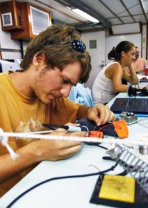 Nathan solders customized expanded battery packs into SPOT GPS units aboard R/V F.G. Walton Smith to compensate for the extended transmission time required by the GLAD experiment. (Photo credit: Tamay Özgökmen)