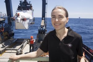 Here, Dr. Samantha “Mandy” Joye is on a field expedition in the Gulf of Mexico. To her left is the legendary research submarine Alvin that she recently used to study the mile-deep seafloor near the Macondo well site. In the background is an oil rig. (Photo provided by Samantha Joye)