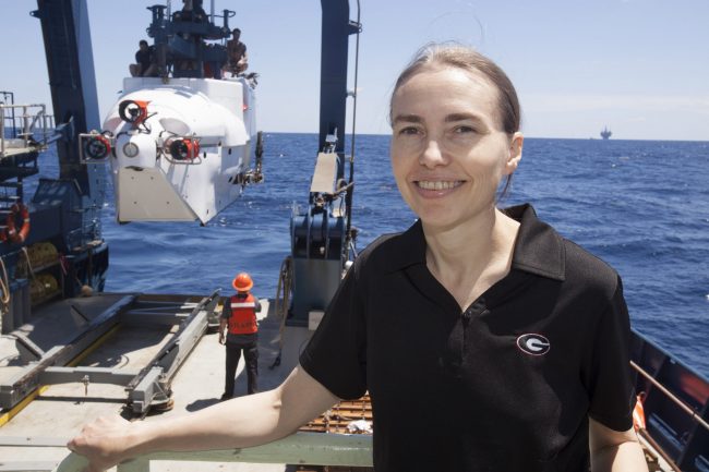 Joye Profile pic 2014 Here, Dr. Samantha “Mandy” Joye is on a field expedition in the Gulf of Mexico. To her left is the legendary research submarine Alvin that she recently used to study the mile-deep seafloor near the Macondo well site. In the background is an oil rig. (Photo provided by Samantha Joye)