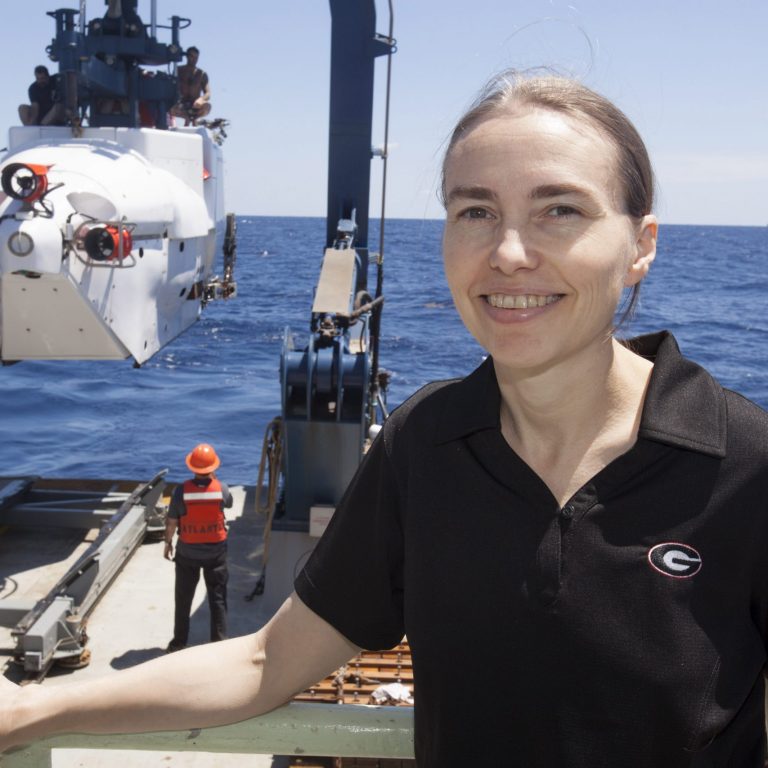 Here, Dr. Samantha “Mandy” Joye is on a field expedition in the Gulf of Mexico. To her left is the legendary research submarine Alvin that she recently used to study the mile-deep seafloor near the Macondo well site. In the background is an oil rig. (Photo provided by Samantha Joye)