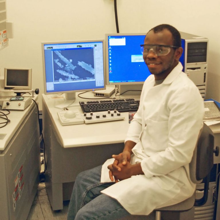 SehindeHeadline-FEATURED_ Sehinde, at the Tulane University Coordinated Instrumentation Facility, sits beside the scanning electron microscope he uses to image halloysite nanotubes and oil droplets stabilized by them. (Photo by Chike Ezeh)