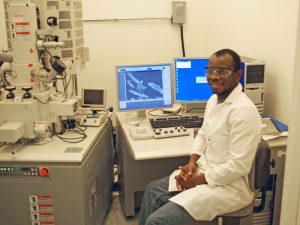 Sehinde, at the Tulane University Coordinated Instrumentation Facility, sits beside the scanning electron microscope he uses to image halloysite nanotubes and oil droplets stabilized by them. (Photo by Chike Ezeh)