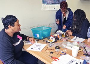 Julian DeRouen (far right), an advanced physics student from Warren Easton Charter High School, shows Fifth Ward Elementary’s Rhodie Simms and West St. John Elementary’s Angela Farnell how to assemble the electronics for their glider models. (Photo by Sara Heimlich)