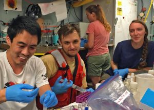 (L-R) Guang-Chao Zhuang, Andy, and Cathrine Shepard share a joke while processing water column geochemistry samples in the main lab of the R/V Endeavor, summer 2017. (Photo provided by ECOGIG)