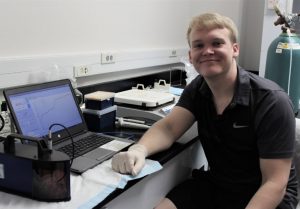 Charles Bergen, a Marine Biology senior at Texas A&M Galveston, measures surface tension on EPS samples from ADDOMEx mesocosm experiments. Samples are placed in a small cup into the tensiometer (lower left). The instrument is sensitive to the force required to withdraw a probe out of the surface of the sample, which is monitored in real time using software on the laptop. Photo by Kathy Schwehr.