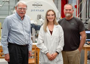 (L-R) Dr. Alan Marshall, Sydney Niles, and Dr. Ryan Rodgers stand in front of the 21 Tesla FT-ICR MS used to analyze photo-oxidized oil samples. (Provided by Sydney Niles)