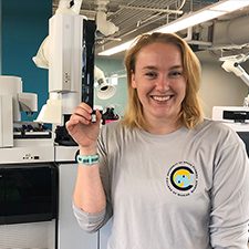 C-IMAGE_Scholar_Schwaab1_slider Madison Schwaab, a University of South Florida master’s student, stands in front of the gas chromatography-tandem mass spectrometer holding an almaco jack liver extract. (Provided by Madison Schwaab)