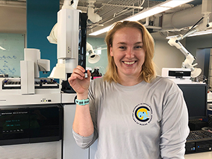 C-IMAGE_Scholar_Schwaab1_slider Madison Schwaab, a University of South Florida master’s student, stands in front of the gas chromatography-tandem mass spectrometer holding an almaco jack liver extract. (Provided by Madison Schwaab)